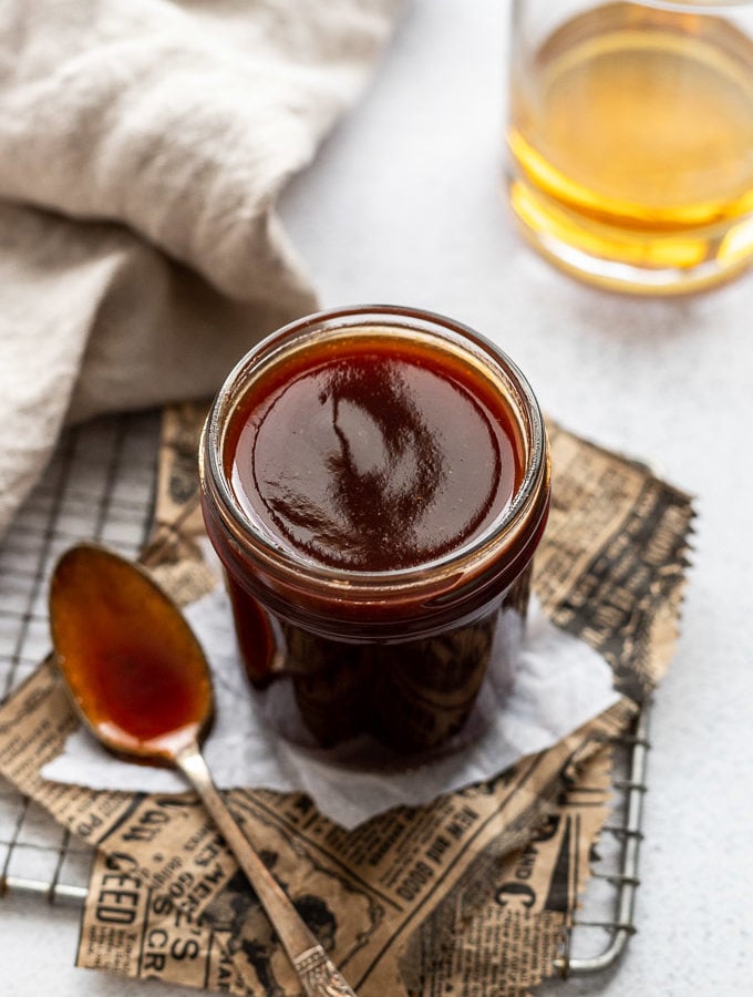 jar of bourbon bbq sauce with spoon and bourbon glass next to it