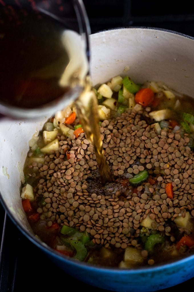 pouring vegetable stock into dutch oven with lentils