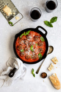 cast iron skillet with vegetarian meatballs and red sauce with parmesan cheese on top