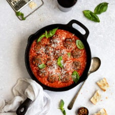 cast iron skillet with vegetarian meatballs and red sauce with parmesan cheese on top