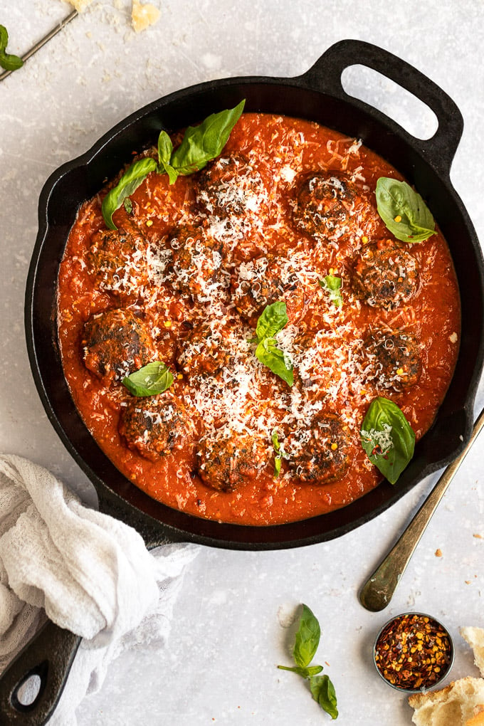 Cast iron skillet with vegetarian meatballs and red sauce with parmesan cheese on top.