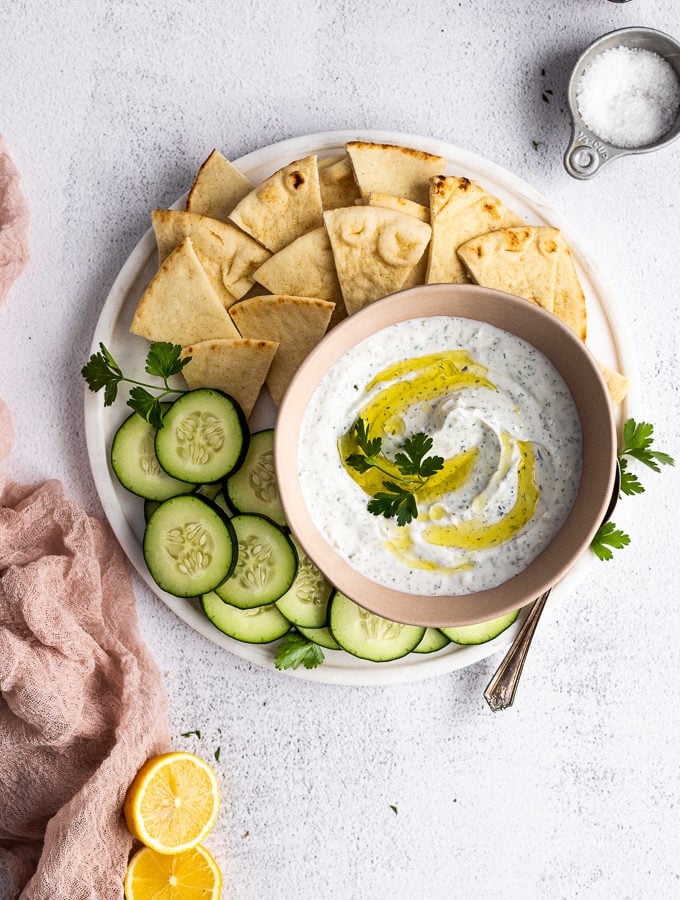 tzatziki sauce on serving platter with cucumbers and pita bread