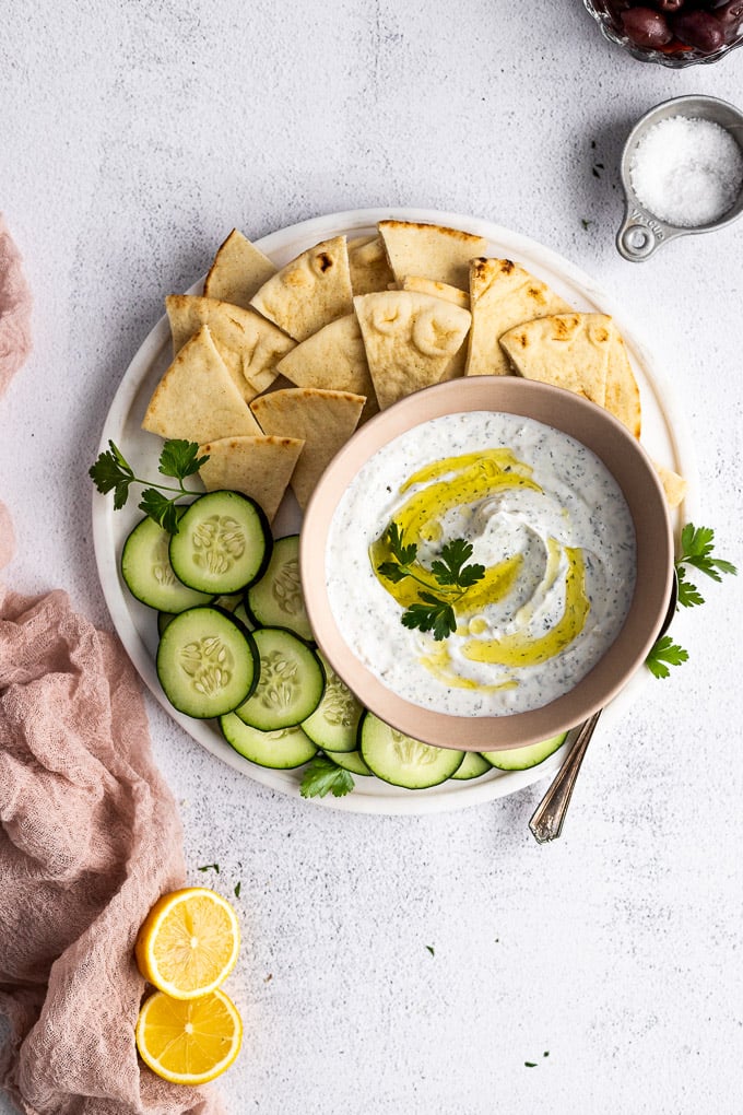 tzatziki sauce on serving platter with cucumbers and pita bread