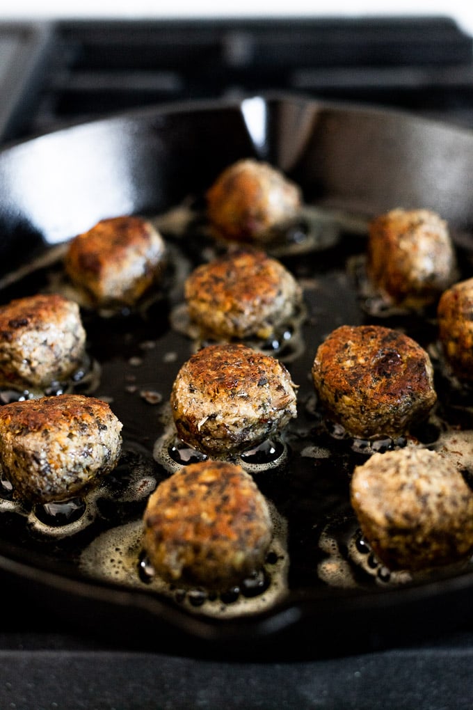 Meatballs cooking in cast iron skillet.