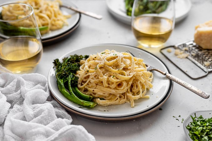 horizontal fettuccine alfredo with roasted broccolini and wine glasses