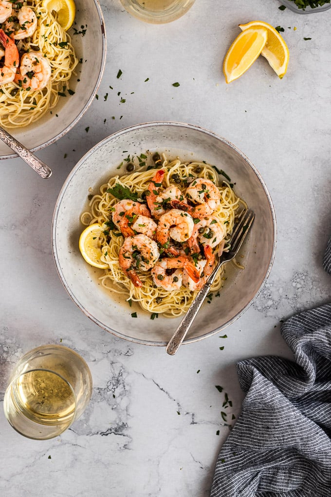 bowl of shrimp picatta with angel hair pasta next to wine glass