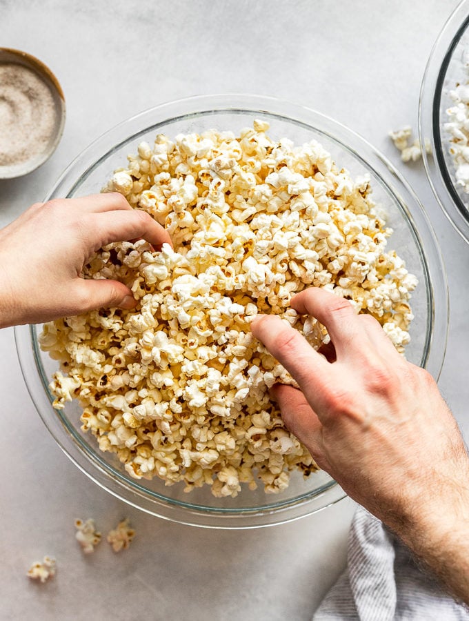 Two hands grabbing popcorn out of a bowl.