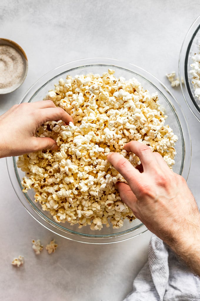 Two hands grabbing popcorn out of a bowl.