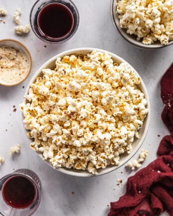Large bowl of popcorn next to smaller one and two wine glasses.