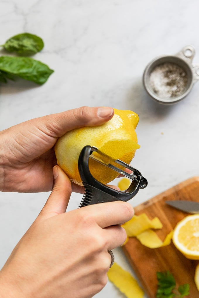 Hand using peeler to peel lemon.