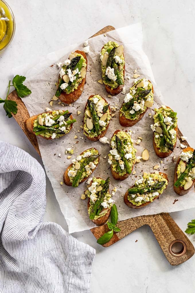 Citrus Pesto Crostini with asparagus and goat cheese crumbles on cutting board.
