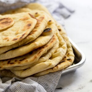 Flatbreads stacked on linen in baking tray.