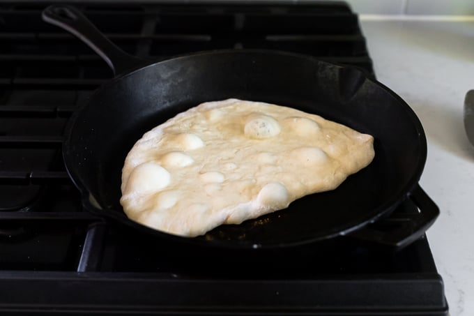 Flatbread dough in cast iron skillet with air pocket bubbles.