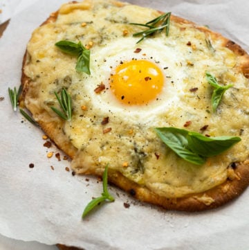 Naan flatbread on parchment paper topped with an egg and basil.