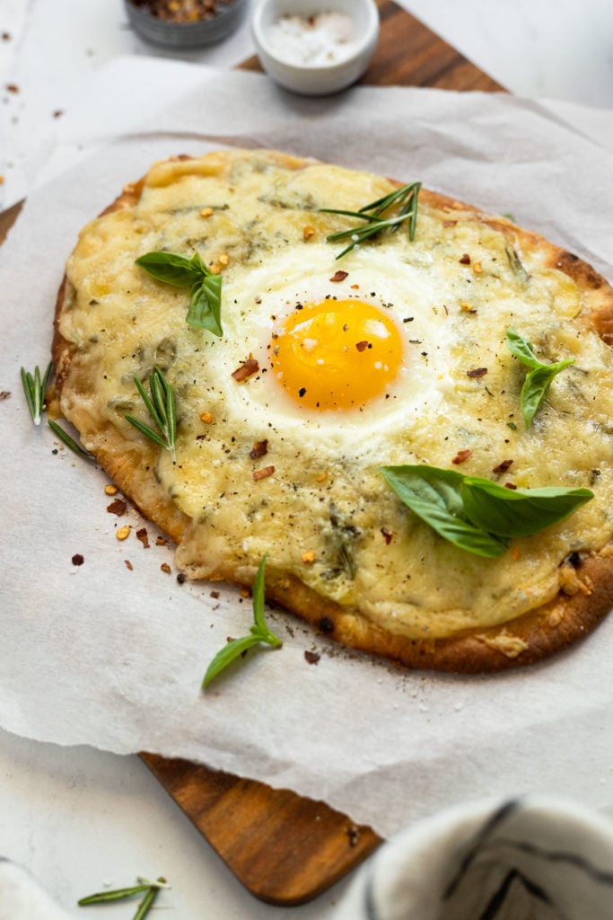 Naan flatbread on parchment paper topped with an egg and basil.