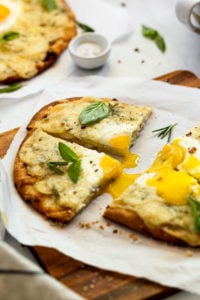 Slices of breakfast pizza with runny egg yolk.