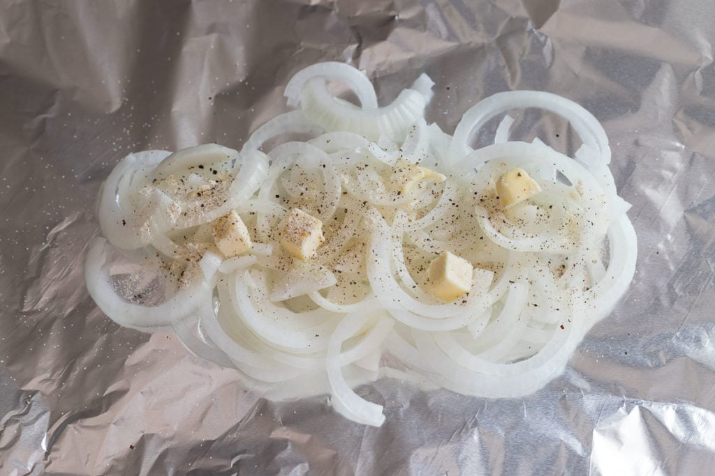 Sliced onions in foil topped with spices and butter.