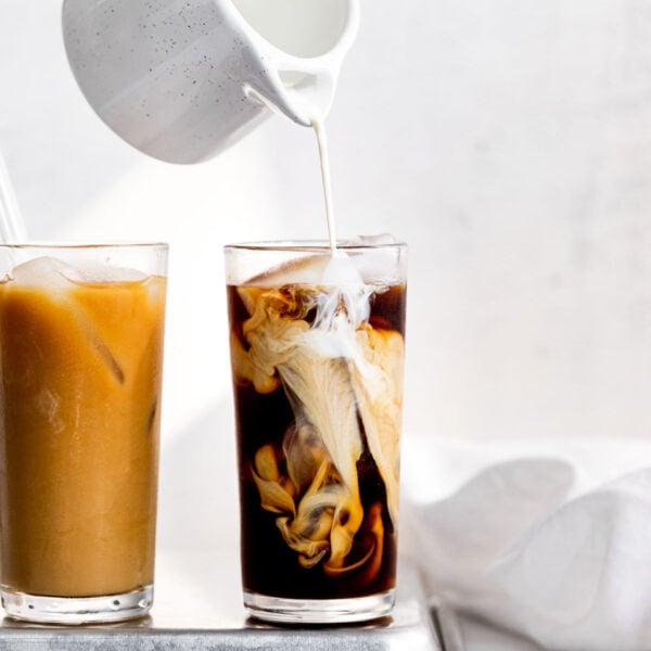 Pouring cream into glass of cold brew next to another glass.