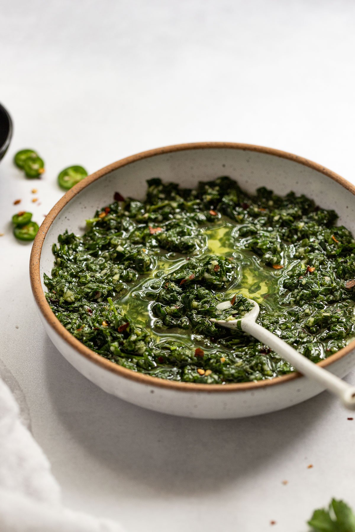Side view of white bowl with chimichurri sauce and spoon.