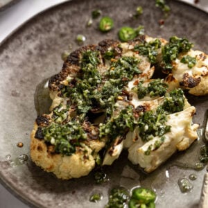 Side view of grilled cauliflower steak with chimichurri sauce on top.