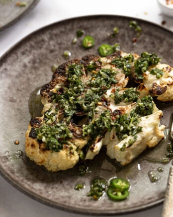 Side view of grilled cauliflower steak with chimichurri sauce on top.