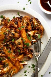 BBQ Cauliflower steaks on a white plate next to knife and fork.