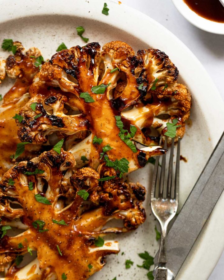 BBQ Cauliflower steaks on a white plate next to knife and fork.