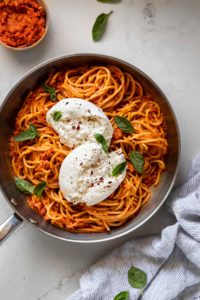 Skillet with romesco pasta topped with burrata cheese.