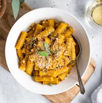 Bowl of rigatoni pasta with fork next to pumpkin and wine.