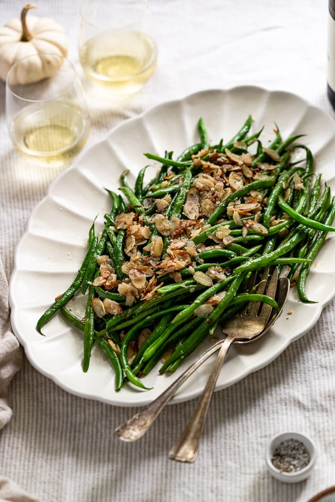 Side view of green beans on platter next to white wine glasses.