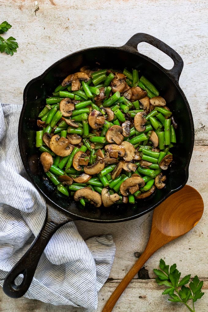 Cast iron skillet with green beans and mushrooms next to spoon.