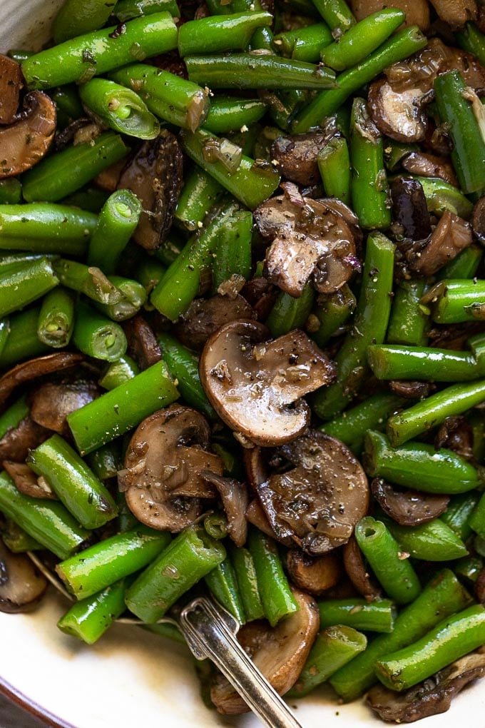 Up close mushrooms and green beans with serving spoon.