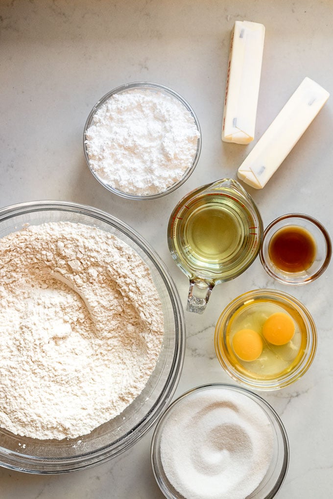 Flour, sugar, oil, butter, eggs, vanilla extract in bowls.