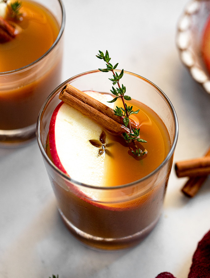 Apple Cider Bourbon Cocktail in glass with apple slice, cinnamon stick, and thyme.