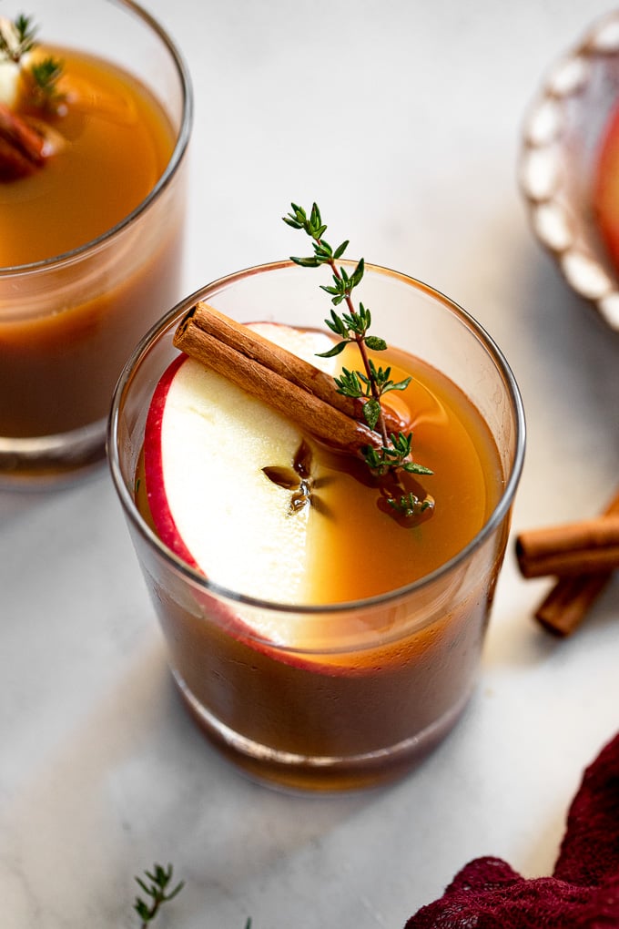 Apple Cider Bourbon Cocktail in glass with apple slice, cinnamon stick, and thyme.