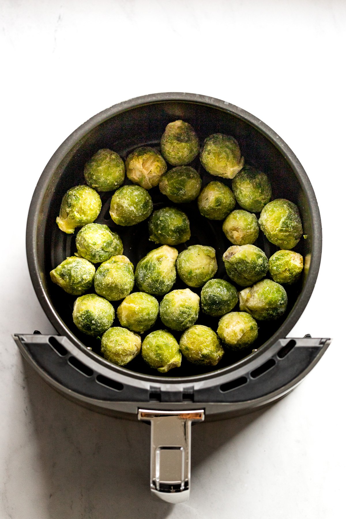 Frozen brussels in air fryer before cooking.