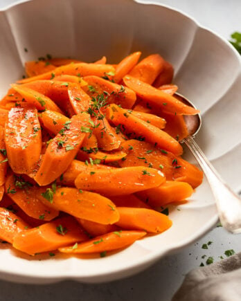 Side view of bowl of steamed carrots with spoon.