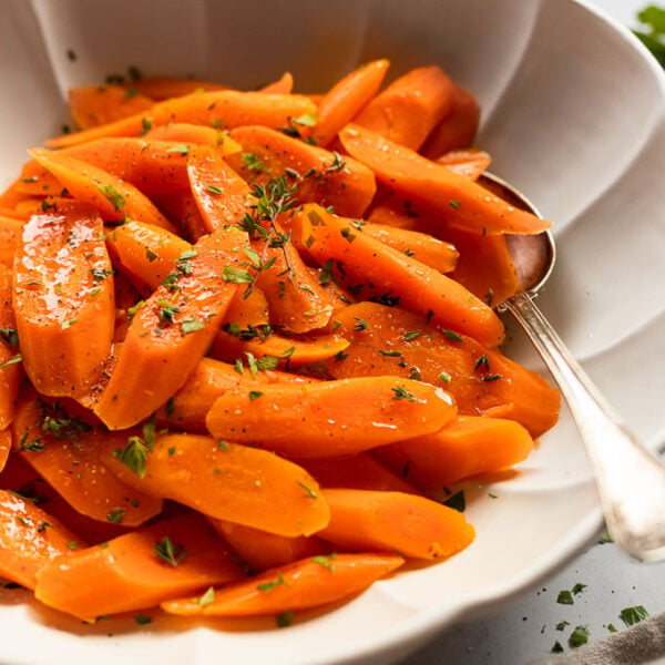 Side view of bowl of steamed carrots with spoon.