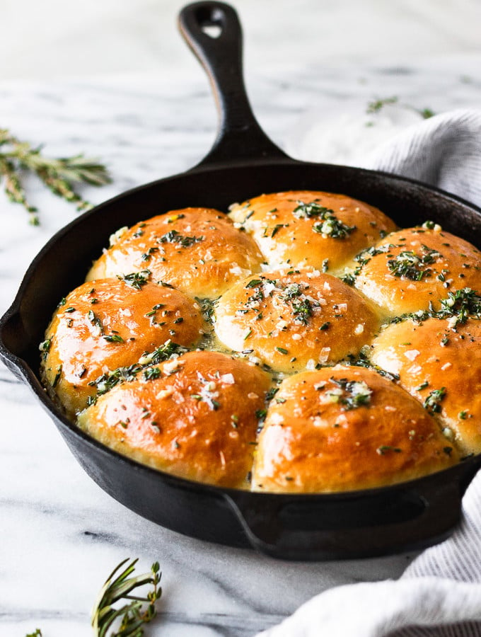 Homemade rolls in cast iron skillet with garlic and herbs on top.