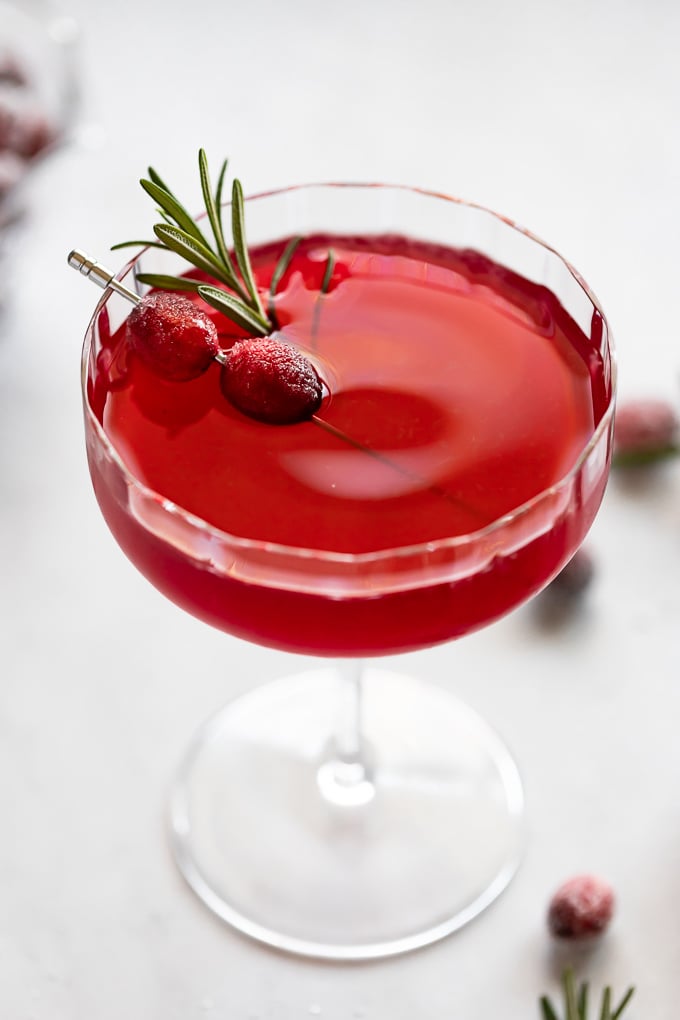 Coupe glass with cranberry cocktail and sugared cranberries as garnish.