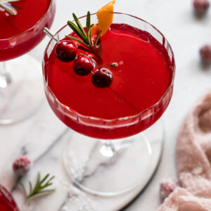 Cranberry ginger cocktail with sugared cranberry, rosemary, and orange garnish.