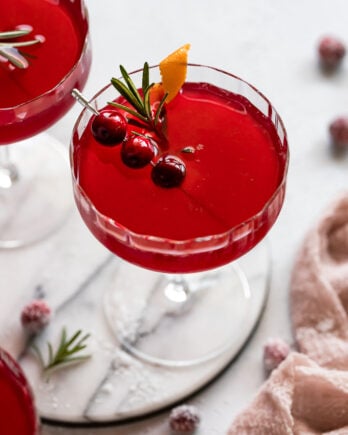 Cranberry ginger cocktail with sugared cranberry, rosemary, and orange garnish.
