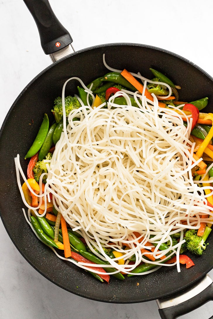 Par-cooked noodles in wok with vegetables.
