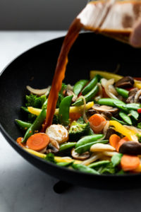 Sauce pouring into wok with mixed vegetables.