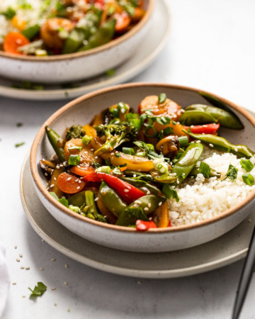 Two bowls of veggie stir fry on plates.