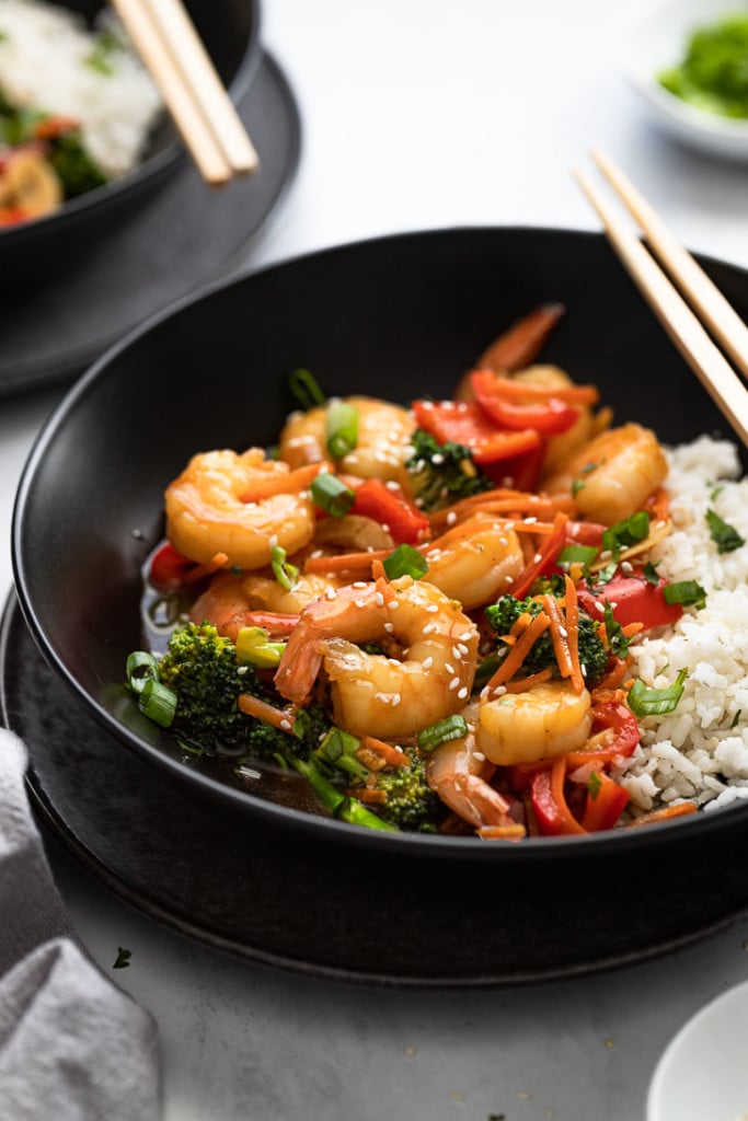 Side view of bowl of shrimp stir fry with chopsticks.