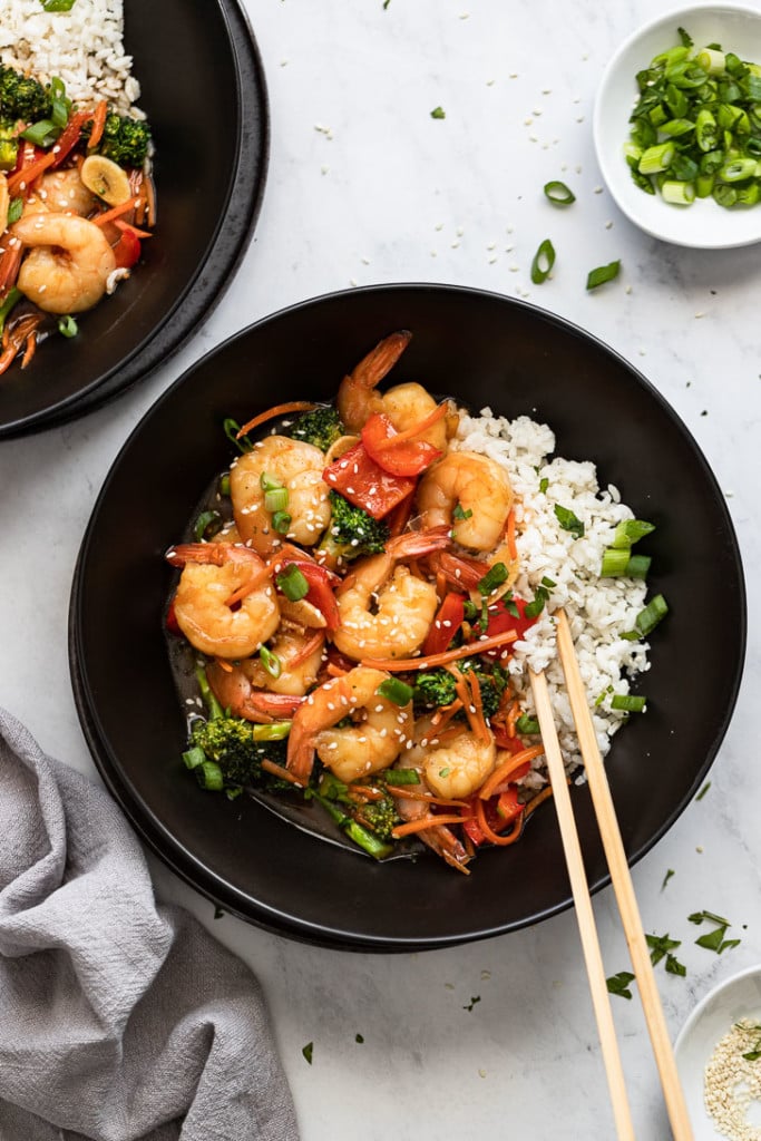 Bowl of shrimp stir fry with rice and chopsticks.