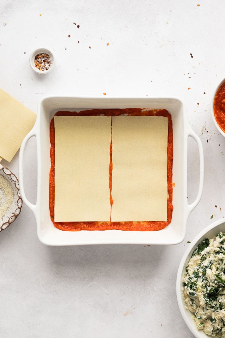 Lasagna sheets on top of sauce in pan.