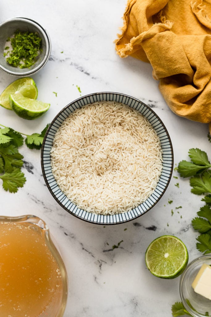 Bowl of rice next to limes and cilantro.