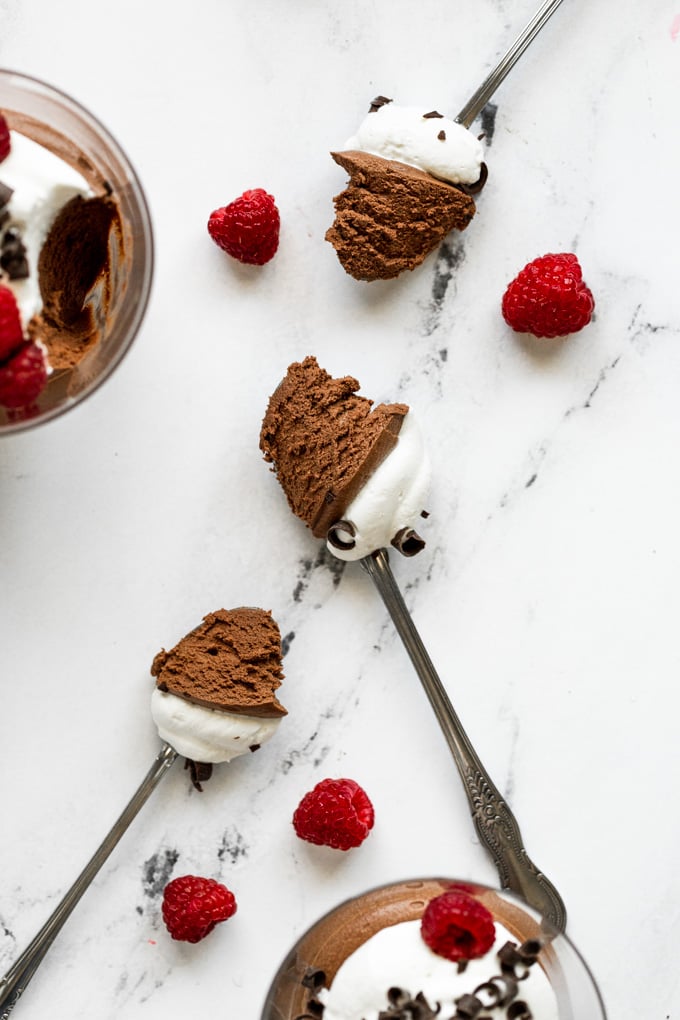 Spoons with chocolate mousse and whipped cream next to raspberries.